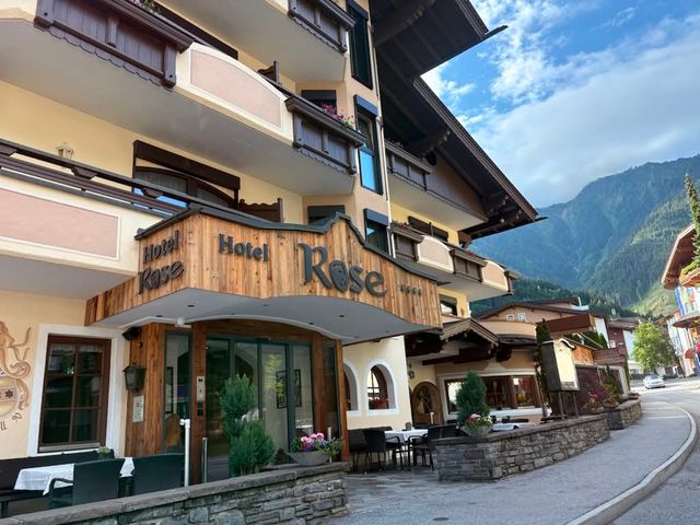 The exterior of Hotel Rose in Austria with a woodsy entrance, balconies above, and mountains in the distance.