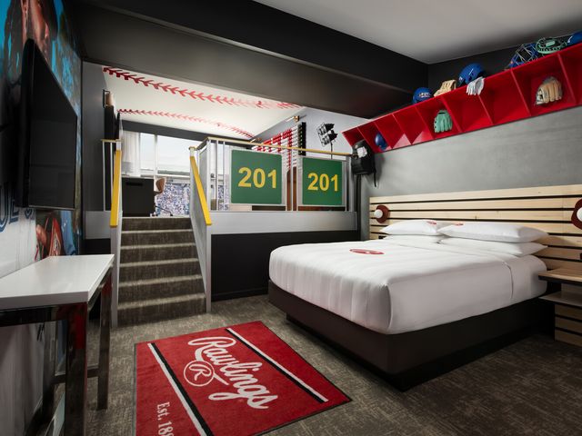 A Rawlings-themed hotel room with red Rawlings-branded. rug and stairs leading to a stadium box.