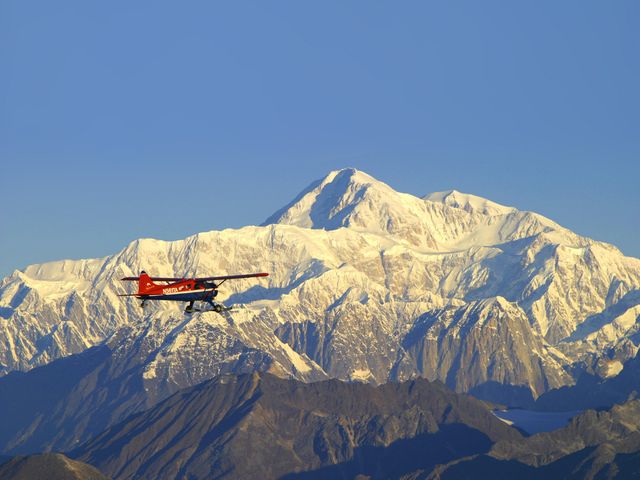 A red helicopter flies next to snow-capped mountains in Alaska