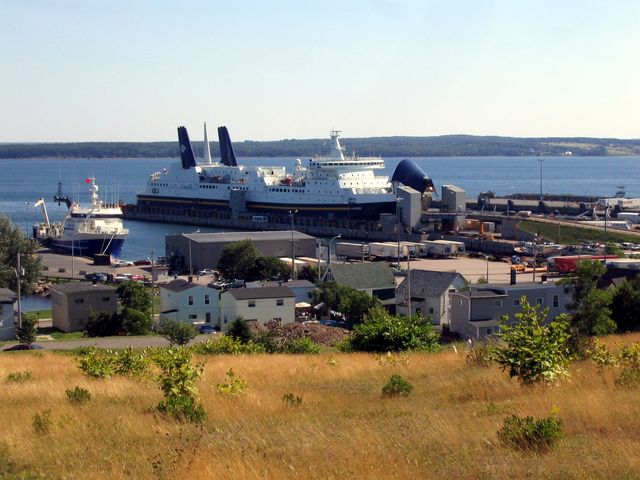 A ship is docked at the harbor in Sydney, Nova Scotia in Canada near a bunch of small buildings.