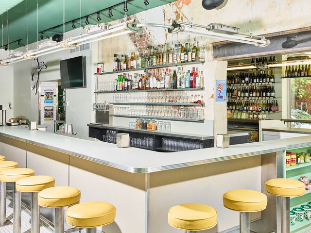 The bar at Supérette in Philadelphia with yellow bar stools, a silver bar, and turquoise accents and shelving.