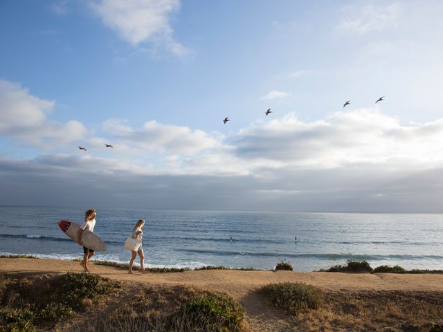 A surfer and a woman walking along the beach in Carlsbad, California.
