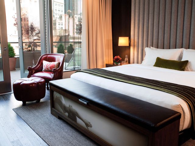 A hotel bed and a red leather chair next to a balcony door at Kimpton Hotel Eventi.