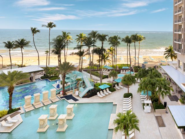 The beach and pool area at San Juan Marriott Resort & Stellaris Casino with lots of pool chairs, palm trees, and part of the hotel visible.