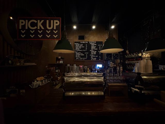 Inside a dimly lit coffee bar with a steel espresso machine and small signs.