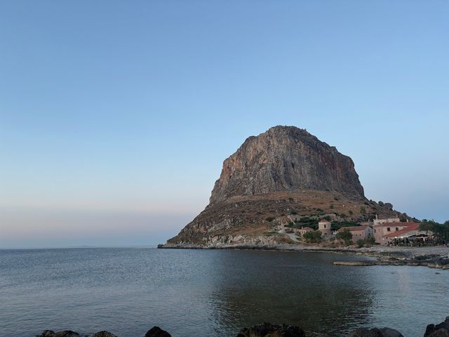 A view of Monemvasia, Greece, as seen from the water with a large mountain and small village.
