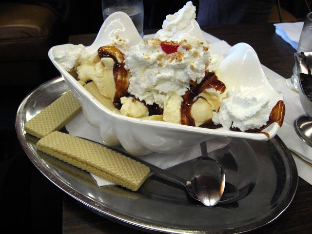 A banana split ice cream sundae in a metal dish with wafers on the tray.