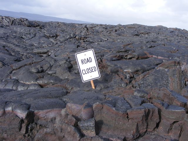 A field of lumpy hardened lava rock and a sign that says road closed.