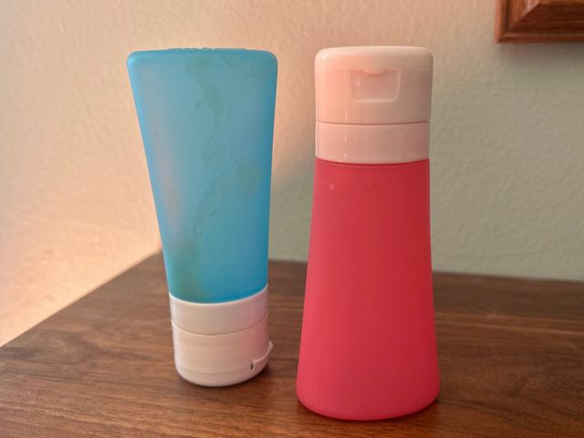 A pink bottle and a blue bottle sit on a wooden table.
