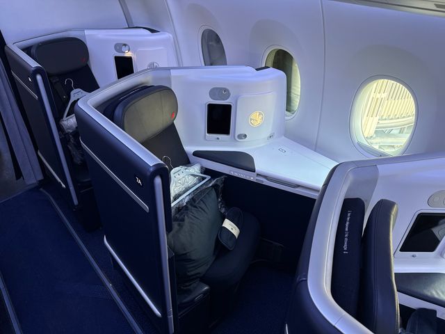 A business class window seat on a cabin on an Air France flight with a hanger and a pillow on the seat.