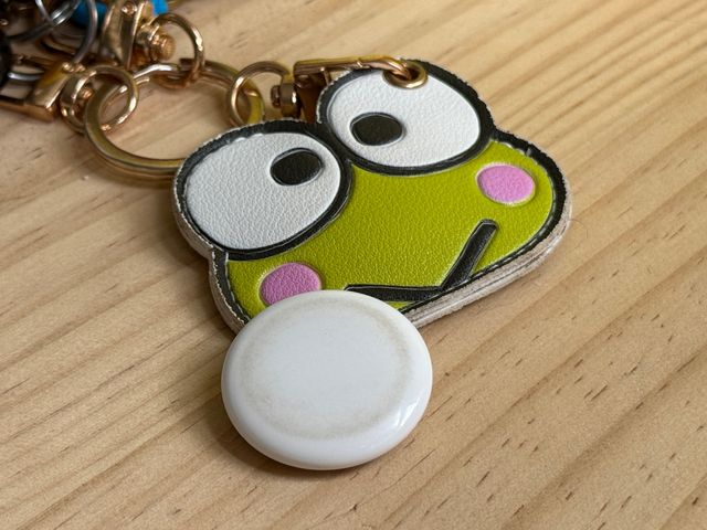 An Apple AirTag attached to a silly front keychain on a wood table.