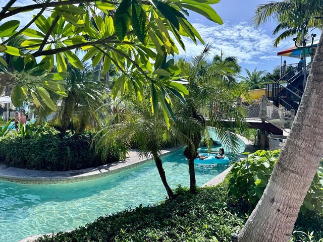 A lazy river is seen through palm trees and lush landscaping at a Beaches Resort.