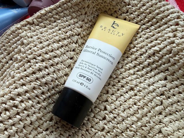 A yellow and white mineral sunscreen on top of a straw beach bag.