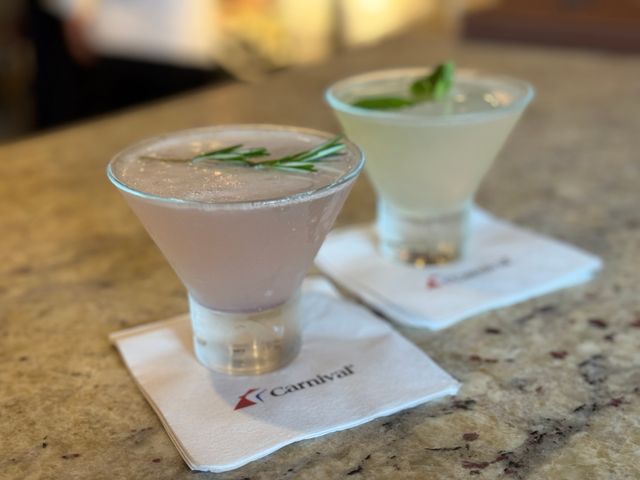 Two cocktails sit on top of Carnival Cruise-branded napkins on a bartop.