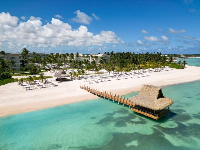 The beach area at the Westin Puntacana Resort & Club with a pier leading out to a thatched hut plus chairs and palm trees on the white sand beach.
