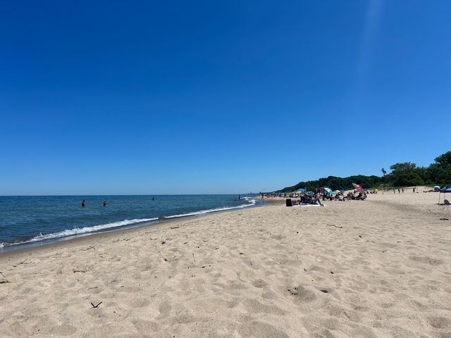 A long sandy beach at Indiana Dunes National Park with people and umbrellas next to the water.