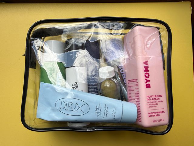 A clear TSA-friendly Packism toiletry bag with beauty and skin products against a yellow background.
