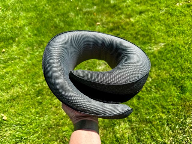 A hand holding a circular travel pillow with grass as a background.