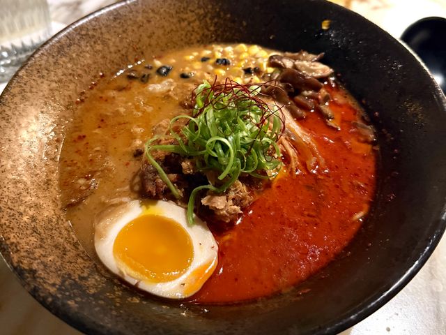 A bowl of ramen with a red sauce on one side and brown on the other and egg in the middle.