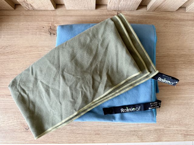 A green microfiber towel on top of a blue microfiber towel, stacked on wood floors.