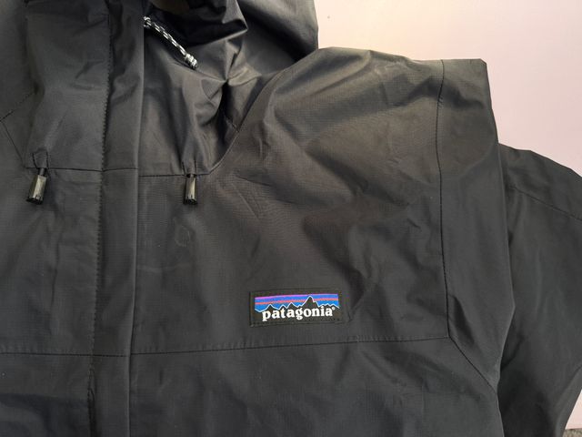 A close view of the logo of a black Patagonia Torrentshell 3L Rain Jacket.