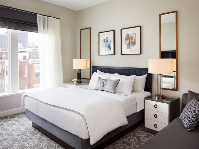 A guest room with a bed and a couch and city views out the window at The Whitney in Boston.