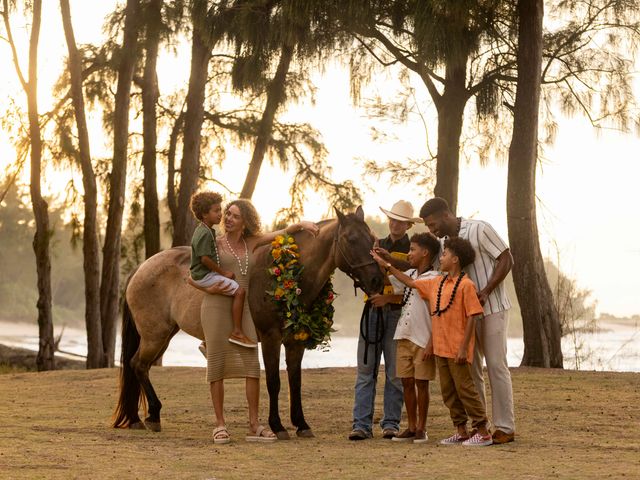 A family pets a horse wearing a lei near the ocean as part of The Ritz-Carlton O‘ahu, Turtle Bay's cowboy luau.