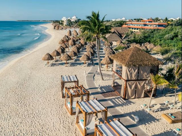 The beach area with thatched umbrellas and cabanas at Iberostar Waves Paraíso Beach in Riviera Maya, Mexico.