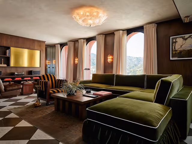 A hotel suite with checkered floors, brown wallpaper, a velvet green couch, and other midcentury furnishings at The Hollywood Roosevelt.