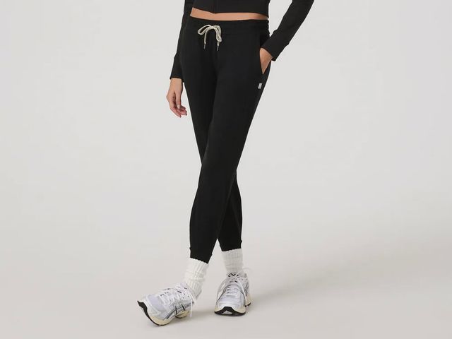 The bottom half of a woman wearing black jogger pants with her feet crossed in front at the ankles.
