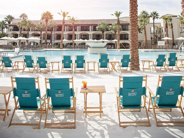 Rows of turquoise beach chairs on a sandy beach area in front of a pool and guest rooms at the Fairmont Scottsdale Princess.