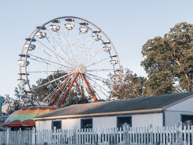 A ferris wheel turns behind a white picket fence and utility building at Playland Park.