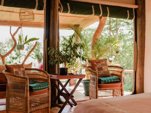 The interior of a cottage with two wicker arm chairs with cushions, a tent-style opening, and a rug and a bed.