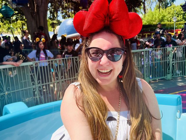 A woman wearing oversized red bow Minnie ears smiles for the camera while on the teacup ride.
