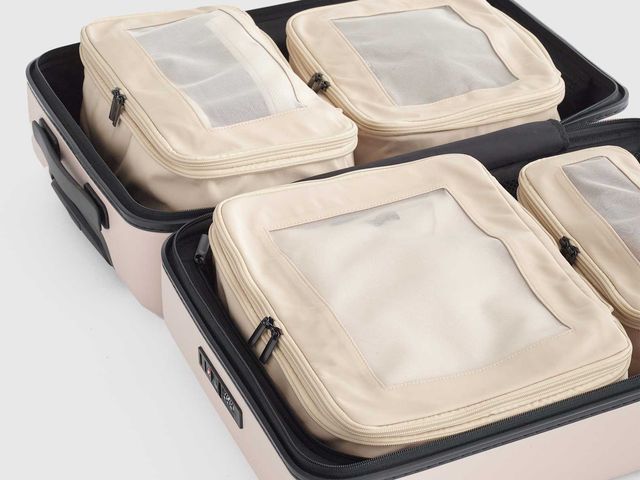 Four beige packing cubes placed inside a pink suitcase against a white background.