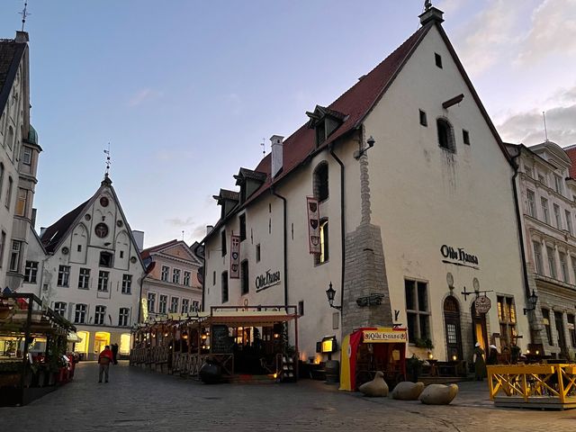 And old white building with pitched brown roof on a cobblestone plaza amidst other medieval buildings