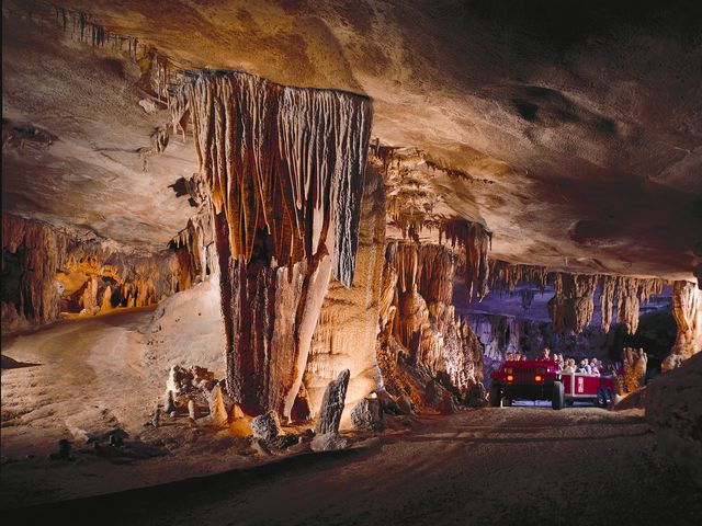 A jeep pulls a tram through an underground cave filled with stalactites and rock formations.