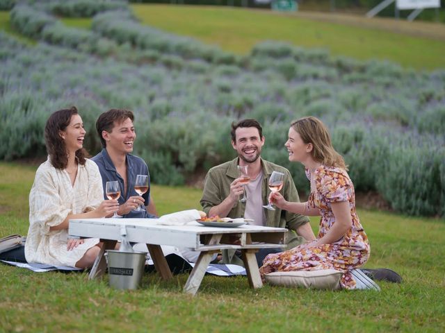A group of friends at Sanctuary at Sirromet sitting at a small picnic table drinking wine in a vineyard.