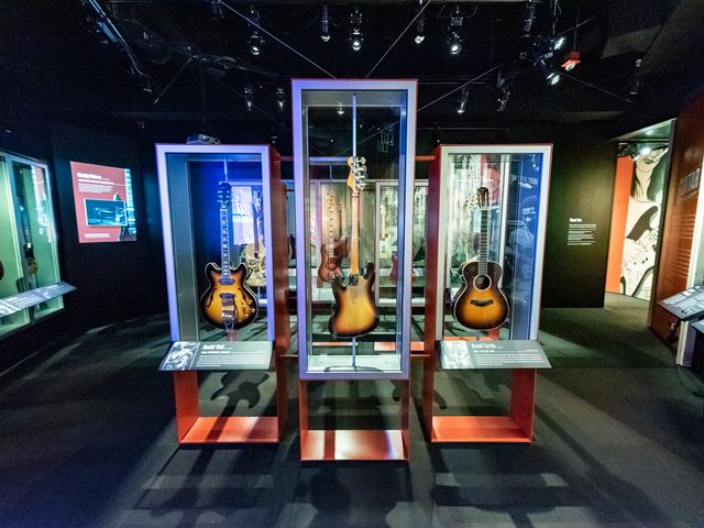 A museum exhibit room with multiple glass cases lit up by neon lights holding guitars.