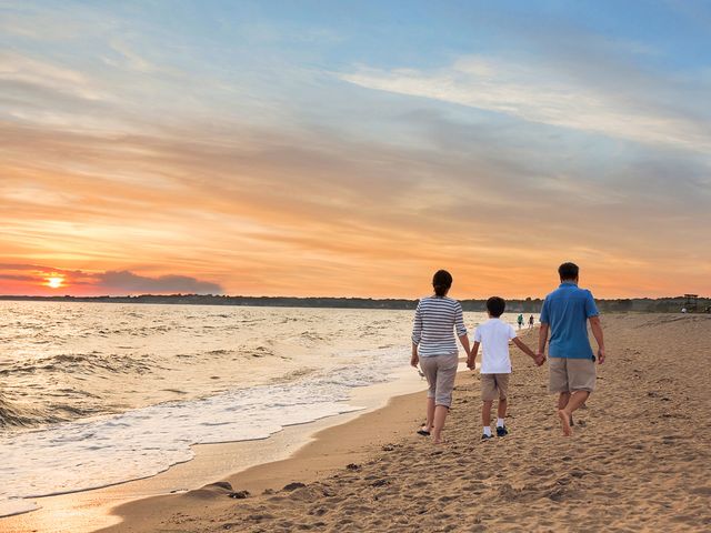 A family of three walks hand in hand on the beach at sunset.