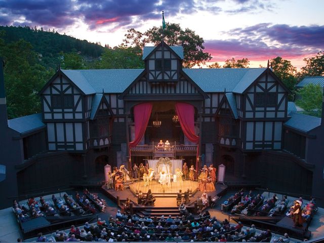 A Tudor-style theatre at dusk with chairs around the stage and a crowd watching a show.