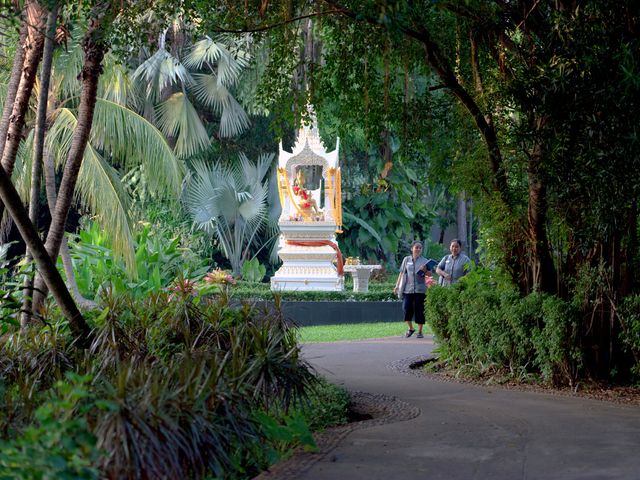 A shrine on a path surrounded by lush trees and greenery with two staff members walking at the JW Marriott Phuket.