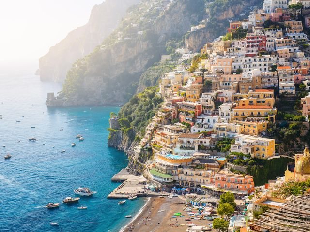 The Amalfi Coast coastline with a hillside full of colorful houses above a small beach with boats in the water.