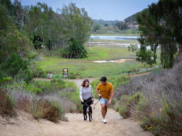 Two people and a dog hiking Batiquitos Lagoon Trail in Carlsbad, California.
