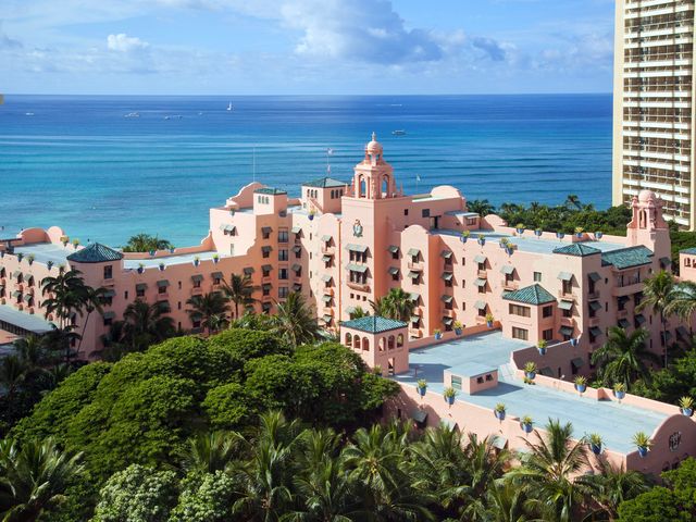 The pink Royal Hawaiian Hotel is seen overlooking the bright blue ocean surrounded by trees