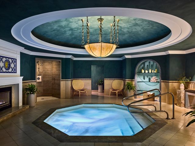 A whirlpool hot tub inside a spa with chairs, a fireplace, and a chandelier.