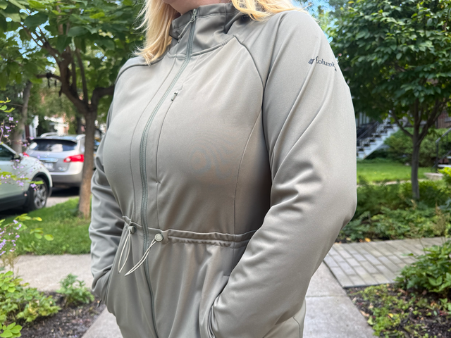 A woman is seen from the neck down wearing a beige jacket that cinches at the waist with a drawstring.