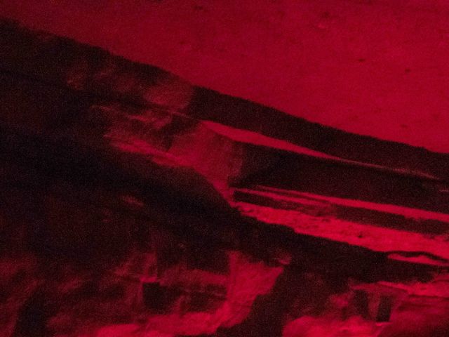 A group tours an underground cave with pink lighting to illuminate what they're looking at.