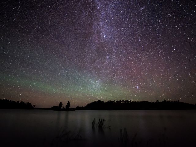 A nighttime sky filled with stars and aurora over a lake in Minnesota.