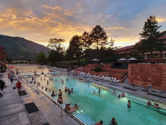 Glenwood Hot Springs' Therapy Pool at dusk with swimmers scattered within the water and a orange-blue sky in the background.